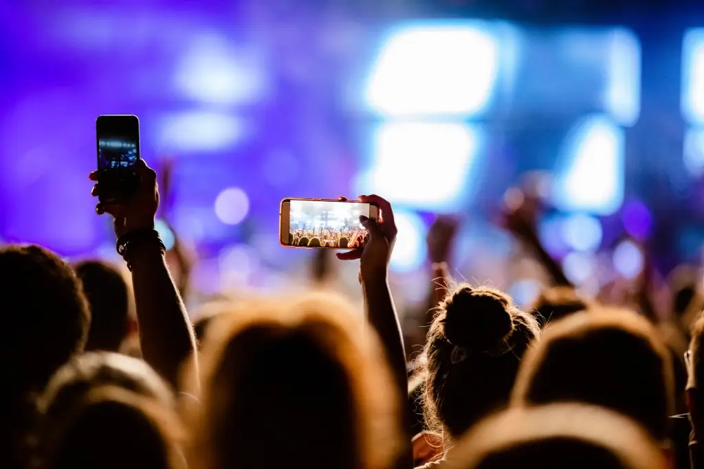 Tangan penonton di konser mengangkat smartphone untuk merekam panggung, menggambarkan bagaimana konten buatan pengguna menjadi bagian penting dari strategi digital marketing.