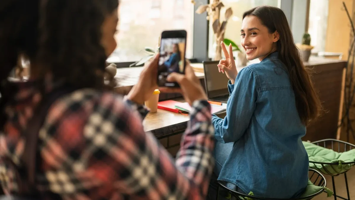 Seorang pelanggan wanita memotret temannya di kafe menggunakan smartphone, ilustrasi nyata dari penerapan strategi User-Generated Content (UGC).