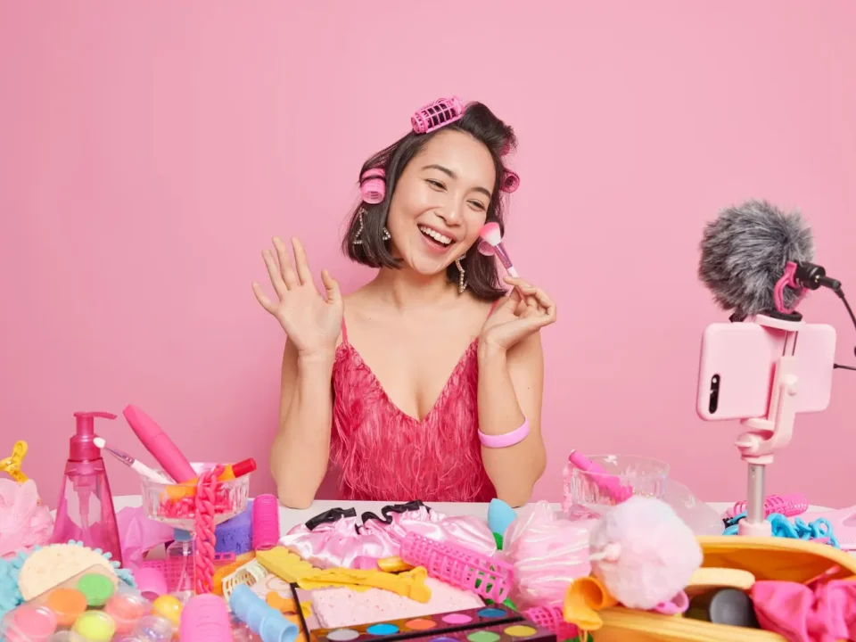 Seorang beauty influencer wanita sedang membuat konten video review produk di depan smartphone, sebuah contoh nyata dari penerapan strategi influencer marketing.