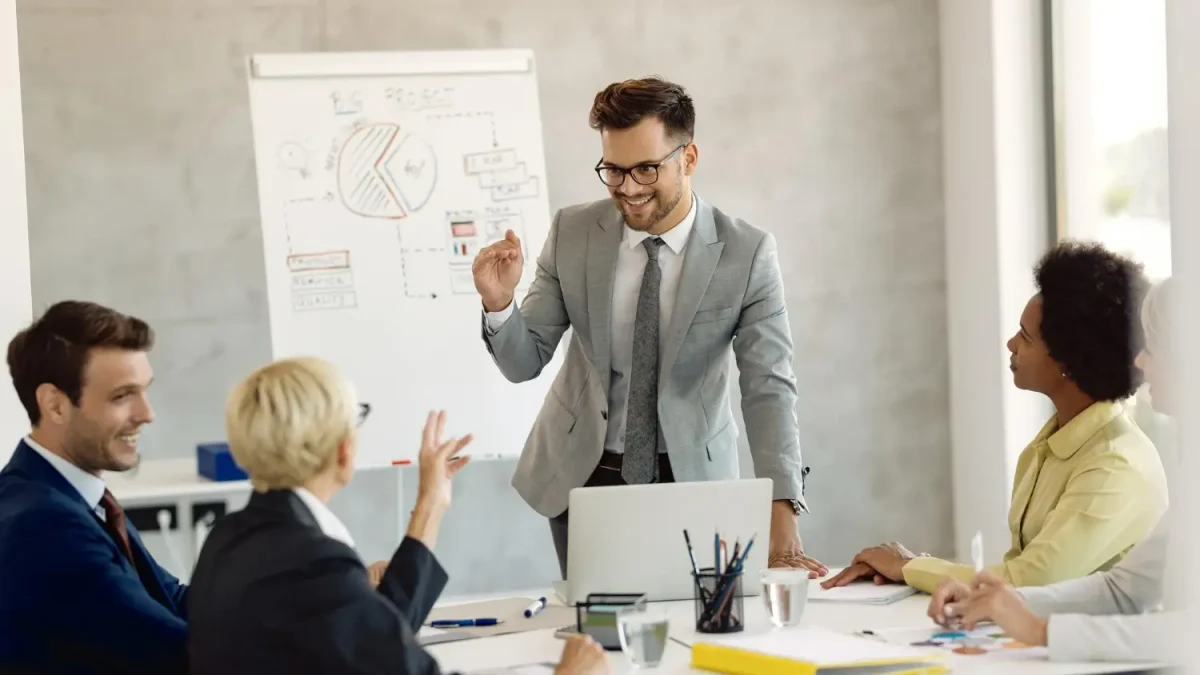 Manajer proyek sedang mempresentasikan strategi di papan tulis kepada timnya, merencanakan penawaran sponsorship event yang komprehensif dan berbasis data untuk menarik sponsor potensial.