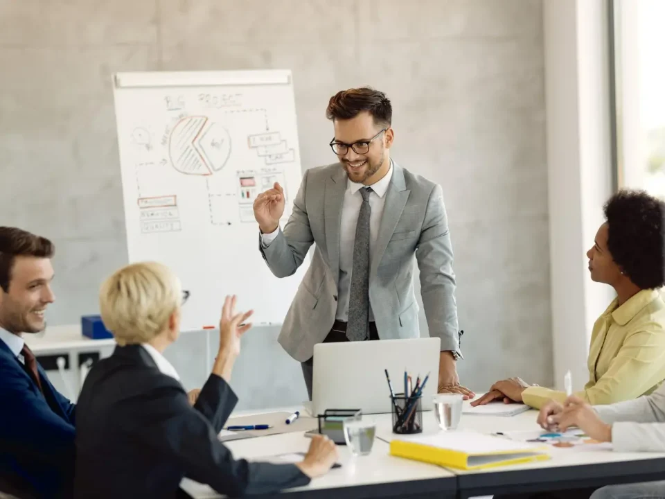 Manajer proyek sedang mempresentasikan strategi di papan tulis kepada timnya, merencanakan penawaran sponsorship event yang komprehensif dan berbasis data untuk menarik sponsor potensial.